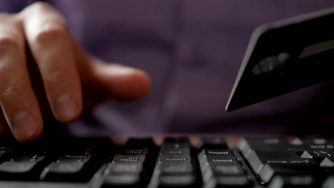 paying with a credit-card online, shopping. male hands with credit card during shopping through internet. computer keyboard. closeup. businessman made an electronic  payment.