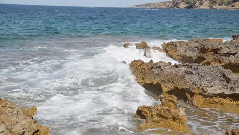 Turquoise-blue-water-white-waves-clashing-onto-rocky-beach-at-Malloca-island