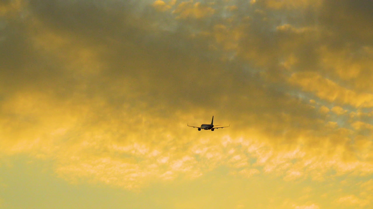 Passenger Jet Airplane in Flight After Takeoff Ascends Into Colorful Sunset Sky With Orange Clouds