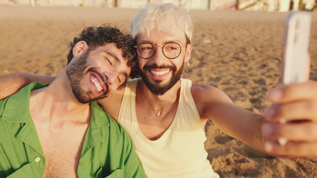 Coppia gay sorridente che si scatta un selfie insieme su una spiaggia sabbiosa