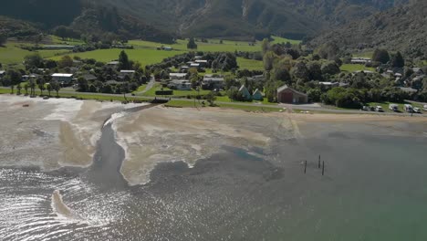 volando sobre el agua del mar con la ciudad de anakiwa en el fondo, sonido de la reina charlotte, sonidos de marlborough, isla del sur, nueva zelanda - antena