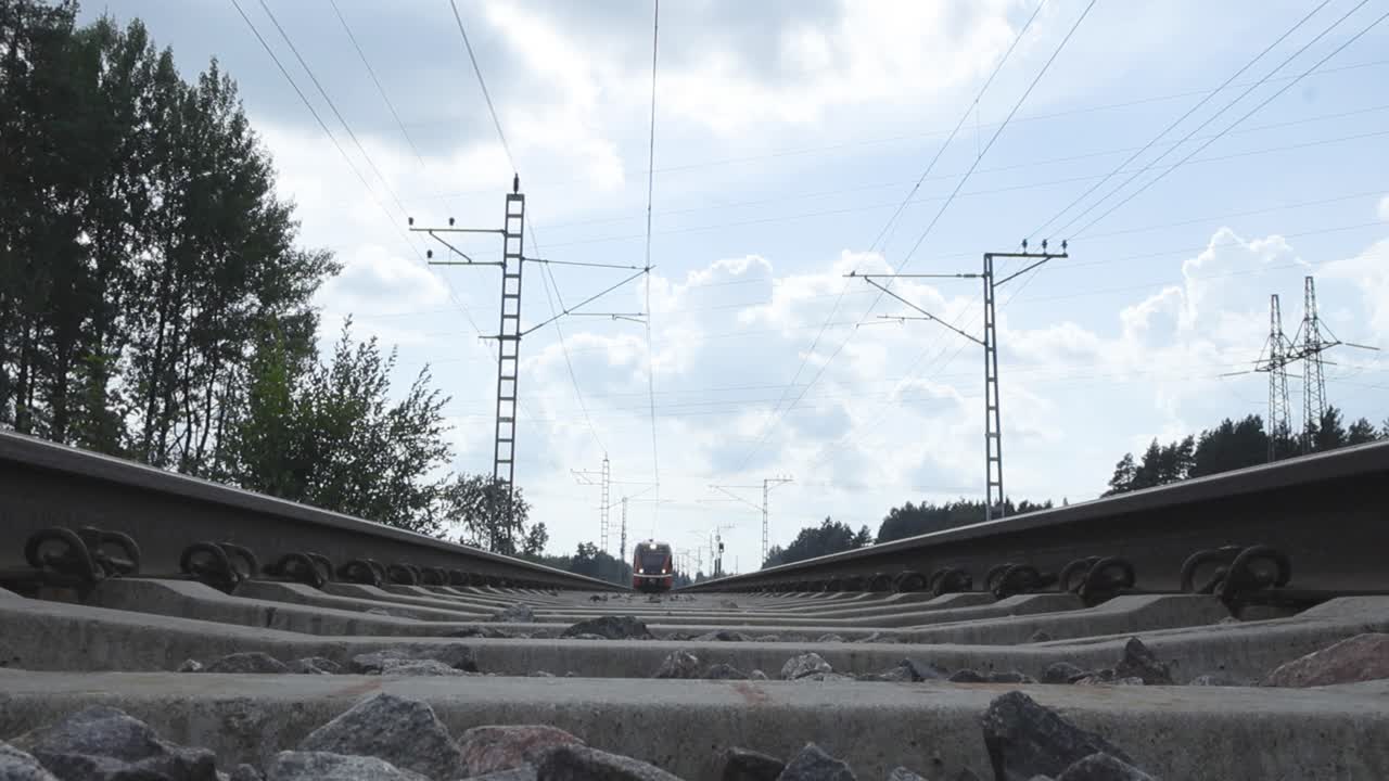 An orange train from the company Elron in Estonia driving over a camera that has been placed on railroad tracks during summertime. Train moves in slow motion, so are the trees on the sides. Cloudy.