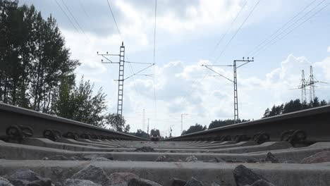 an orange train from the company elron in estonia driving over a camera that has been placed on railroad tracks during summertime. train moves in slow motion, so are the trees on the sides. cloudy.