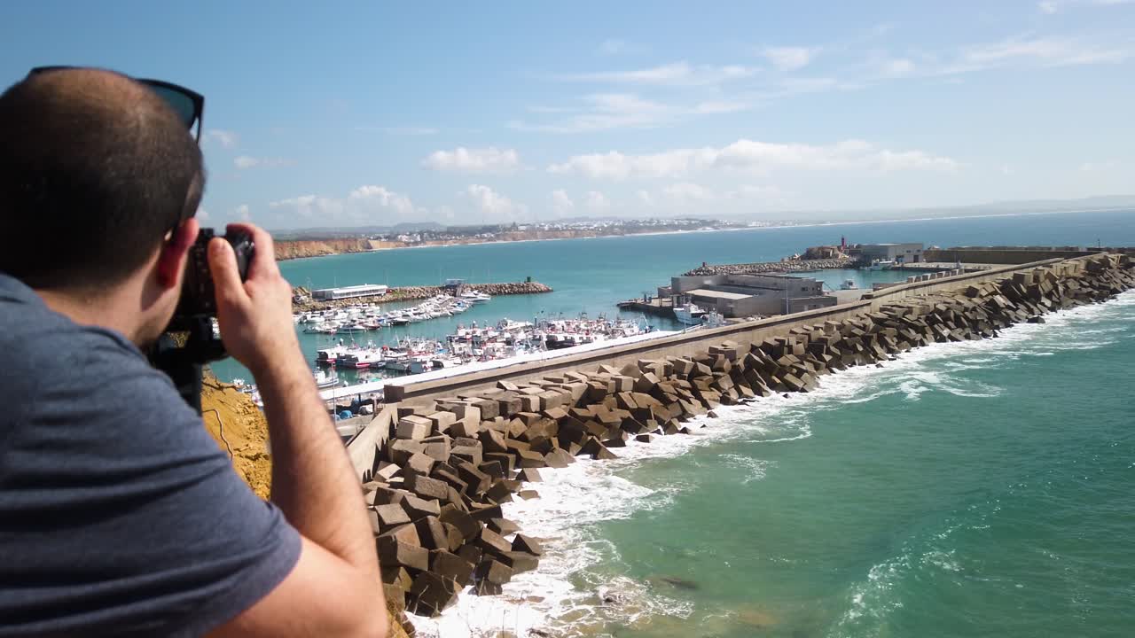 hombre fotógrafo toma fotos del puerto de conil, españa, cámara lenta sobre el hombro