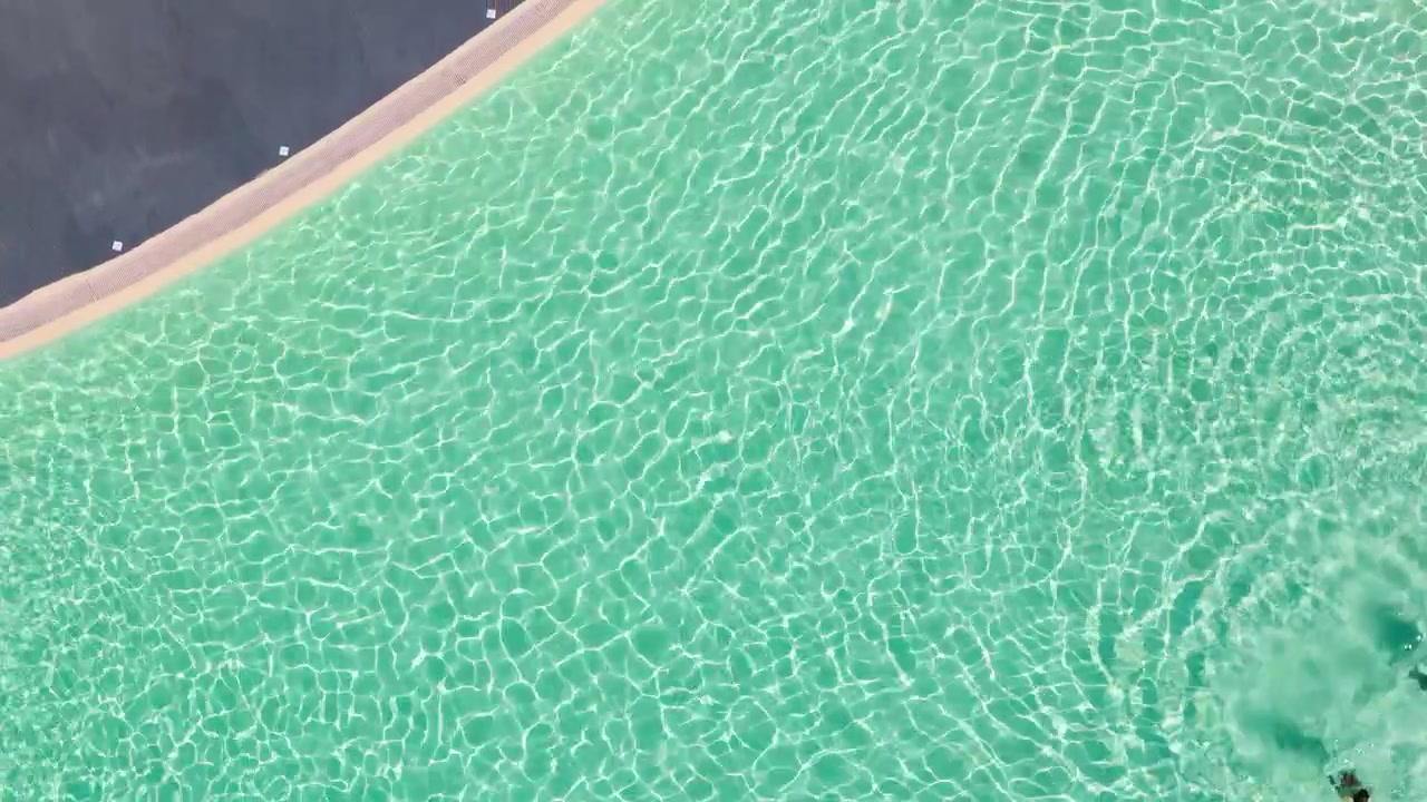 Luftaufnahme eines klaren türkisfarbenen Swimmingpools mit sonnenbeschienenen Wellen und geschwungenem Rand