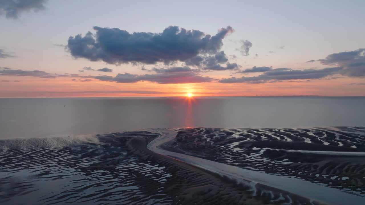 Setting Sun On Horizon Over Calm Irish Sea With Reverse Camera Flight Over Dark Tidal Sand Flats And Inlets. Golden Hour. Fleetwood, Lancashire, UK