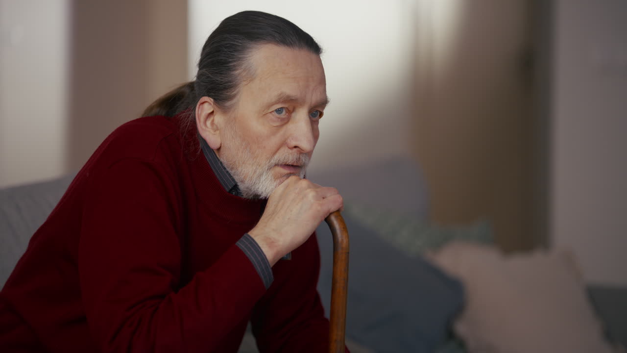 Thoughtful Elderly Man Sitting Indoors with a Walking Stick