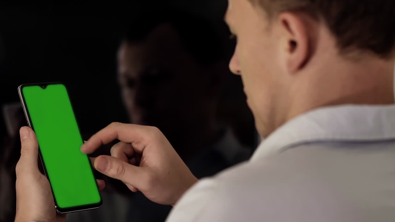 전화를 가진 젊은이가 화면을 가로질러 손가락을 움직이고, 크로마 키, 백 뷰