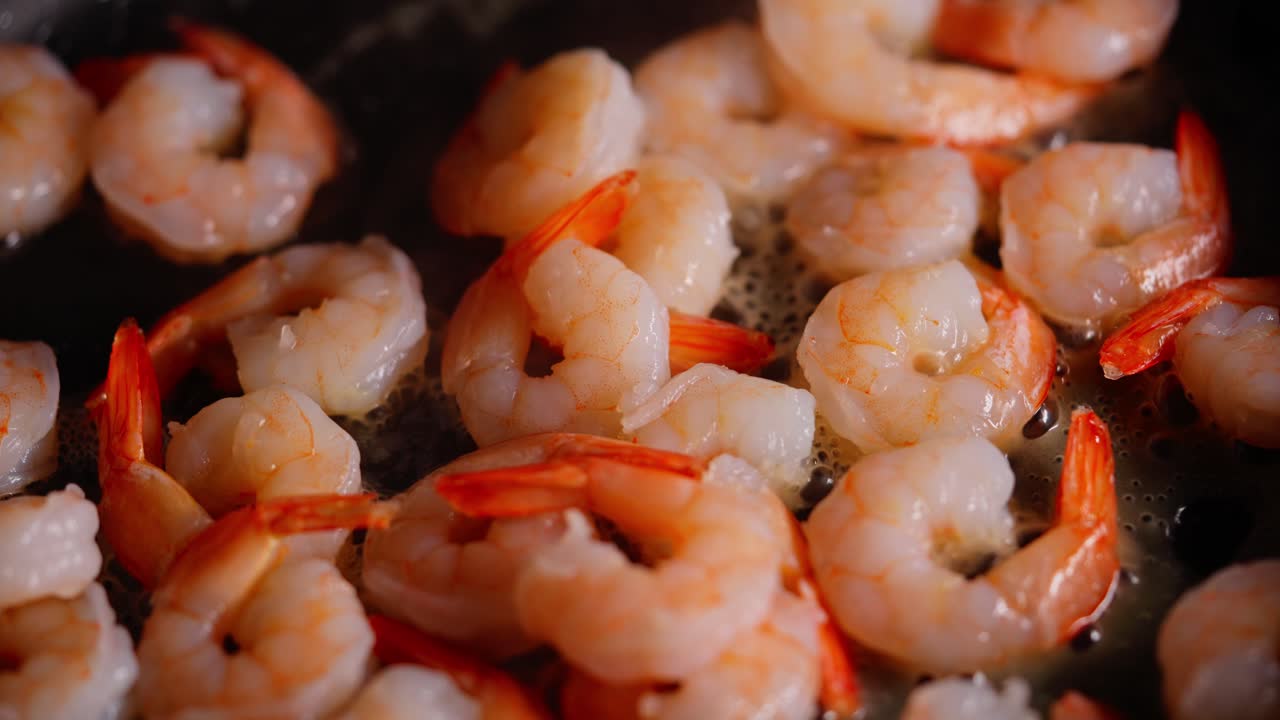 Sizzling shrimp frying in pan with bubbles and oil as they turn pink and golden brown, slow motion