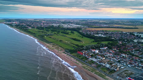 Aerial-drone-footage-displays-Skegness-seaside-town-at-sunset,-featuring-holiday-park,-beach,-sea,-and-caravans-on-sweeping-vistas