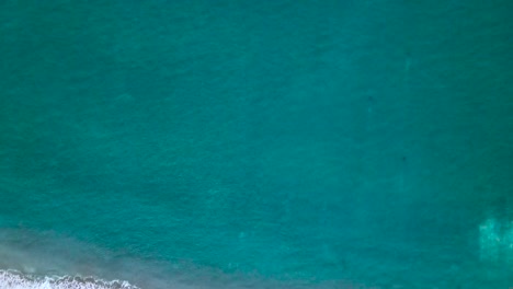 Rising-birdseye-view-of-royal-blue-clear-water-and-sandy-beach-waves