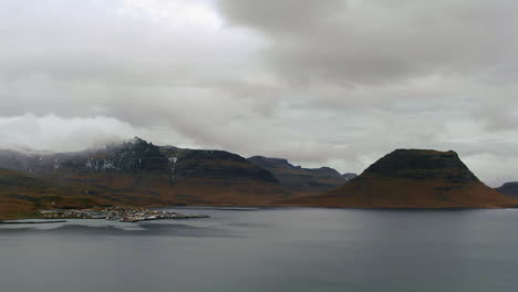 Drone-view-of-a-coastal-community-in-Iceland-with-snow-capped-mountains-in-the-distance