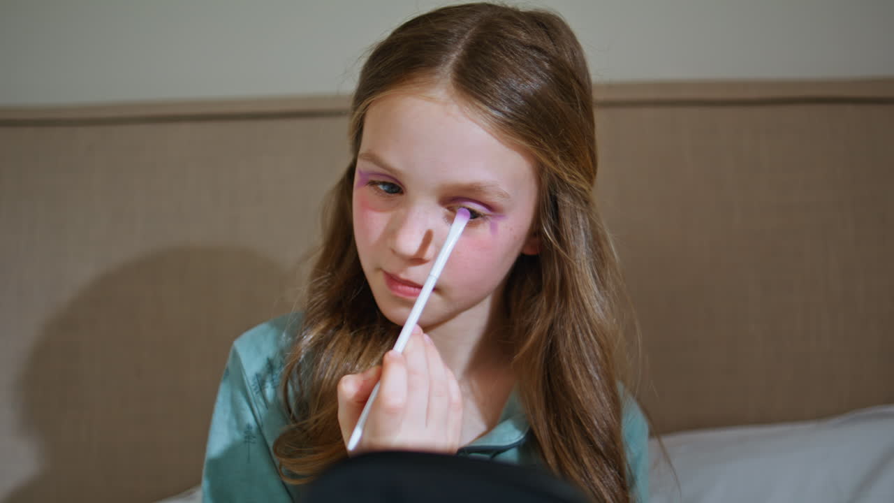 Funny toddler using makeup painting face with shadows. Little kid playing alone