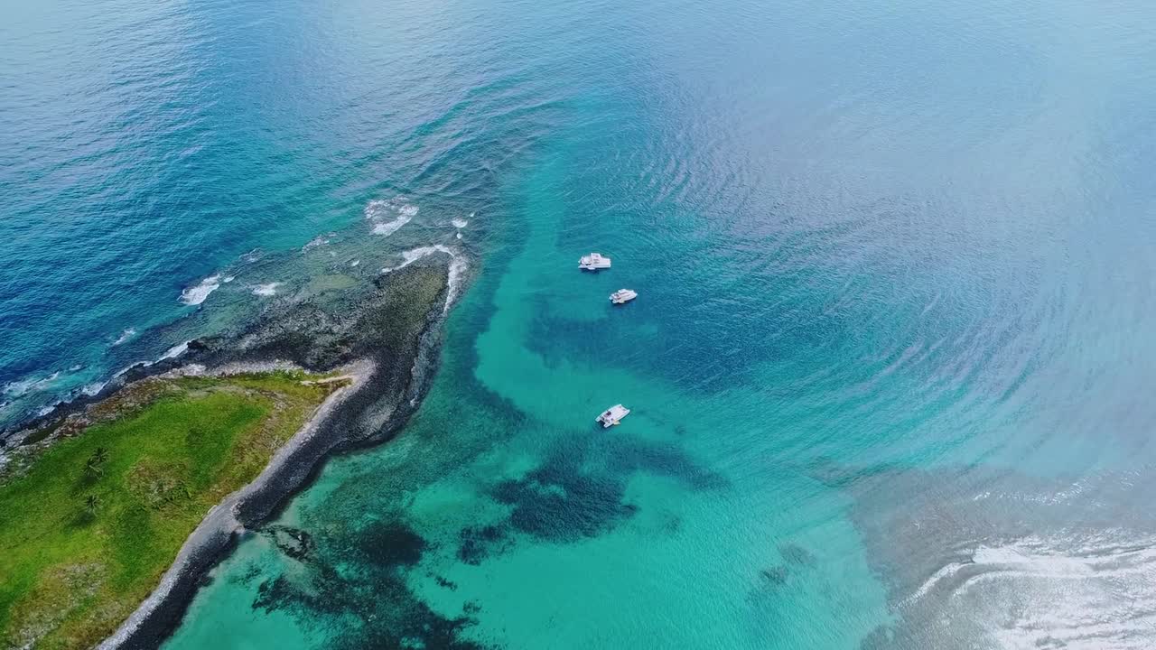 Arcipelago di Abrolhos vicino a Caravelas, Bahia, Brasile, con piattaforma di barriera corallina e acqua turchese poco profonda su substrato vulcanico con barche ancorate all'interno del parco nazionale marino, sorvolo in avanti con drone.