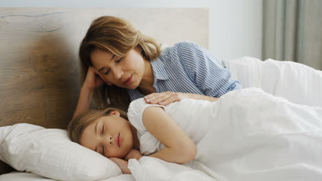 Close-up-view-of-cute-blonde-little-girl-sleeping-on-the-bed-while-hugging-her-teddy-bear