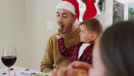 Hijo-Caucásico-Dándole-Comida-A-Su-Padre-Con-Un-Tenedor-Durante-La-Comida-Navideña