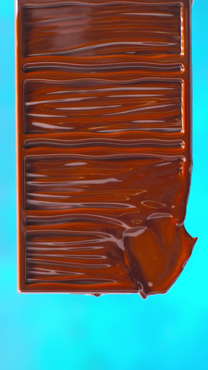 video vertical de primer plano de una barra de chocolate derretida contra un fondo de color azul con espacio para copiar