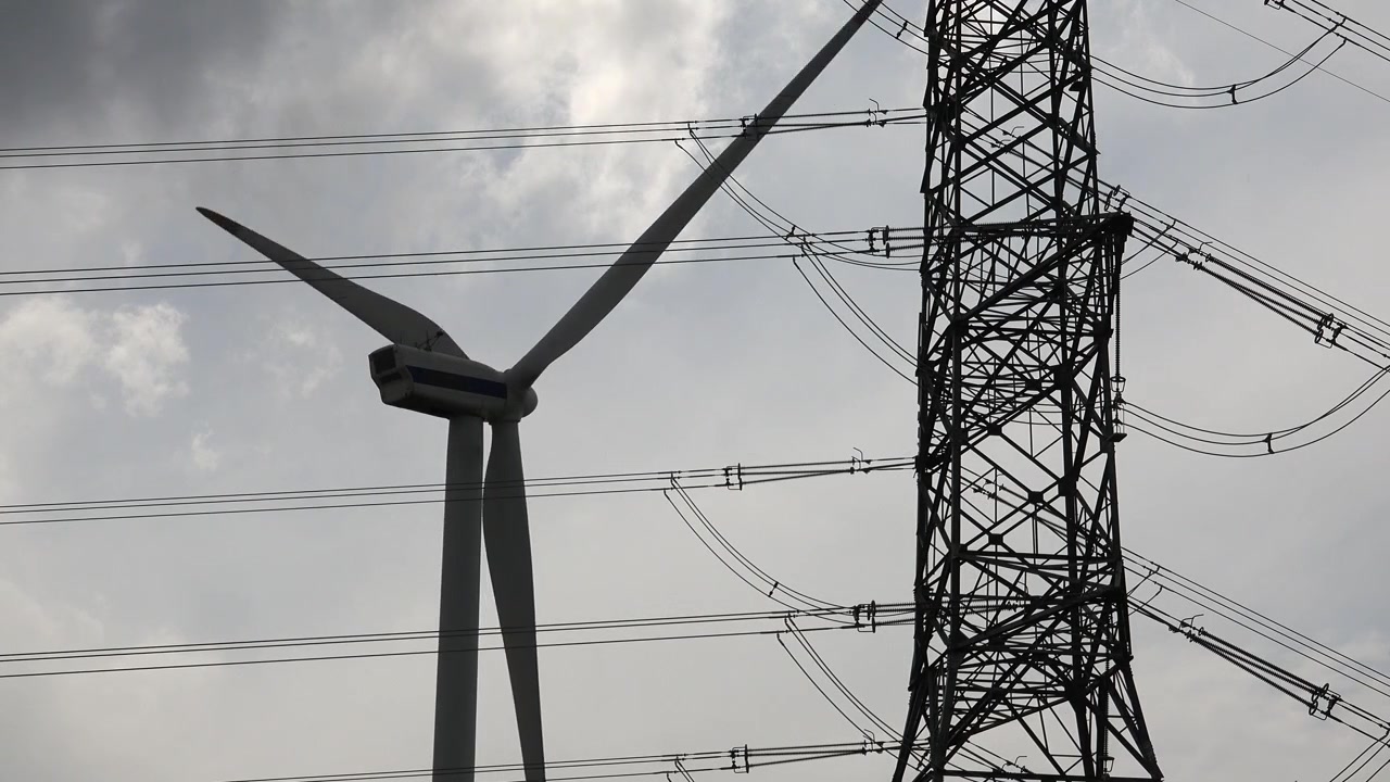 Wind Turbine Rotating Next to High Voltage Power Transmission Tower