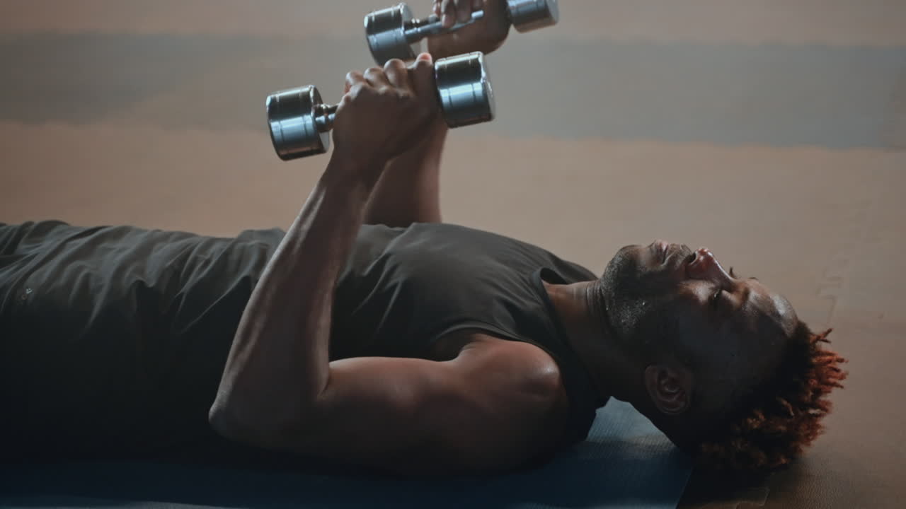 Man performing dumbbell exercises on a mat