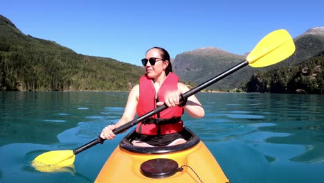 happy female tourist is kayaking lake lovatnet at a beautiful sunny summer day - emerald green glacial lake with mountain background - view from kayak bow including slow paddling camera movements
