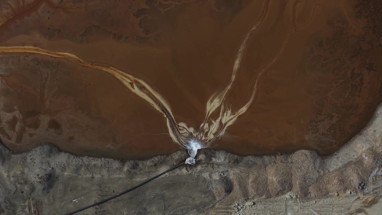 Vue aérienne d'eau polluée brunâtre à côté d'une centrale électrique à combustibles fossiles, montrant des déchets industriels, des eaux usées contaminées et la pollution environnementale