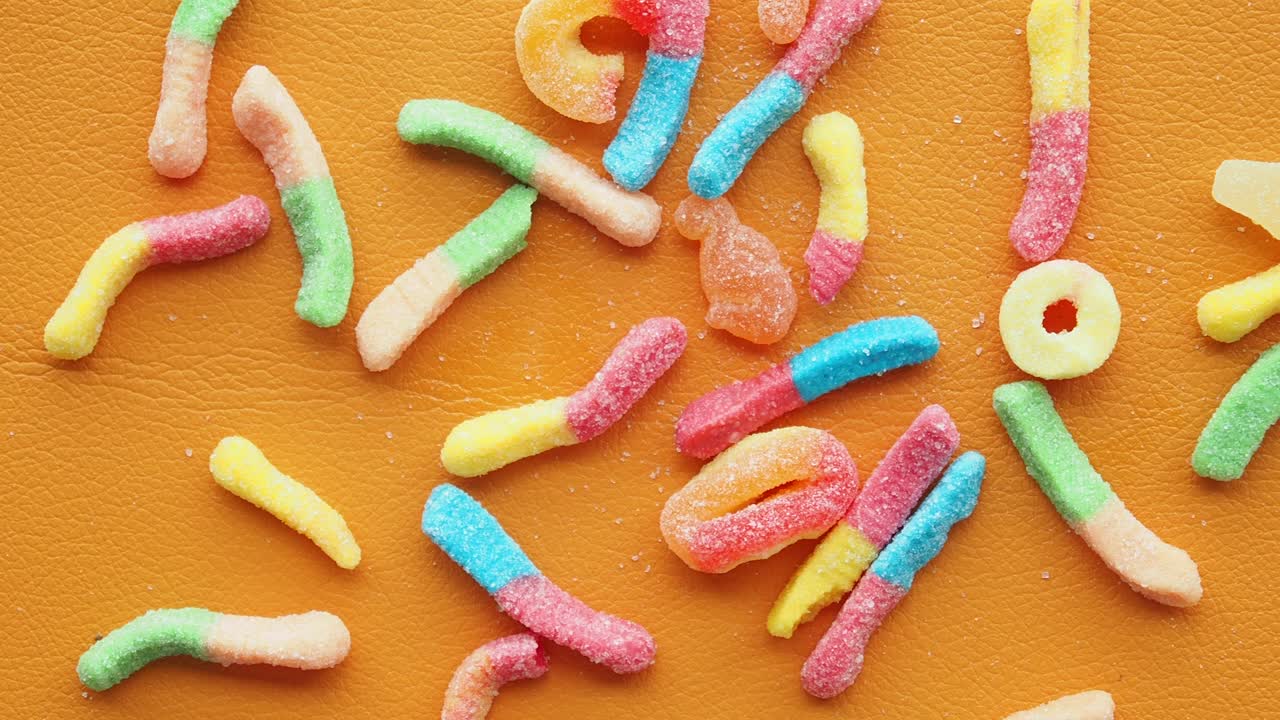 Colorful Gummy Worms and Other Candies on an Orange Surface