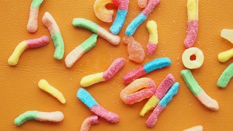 colorful gummy worms and other candies on an orange surface