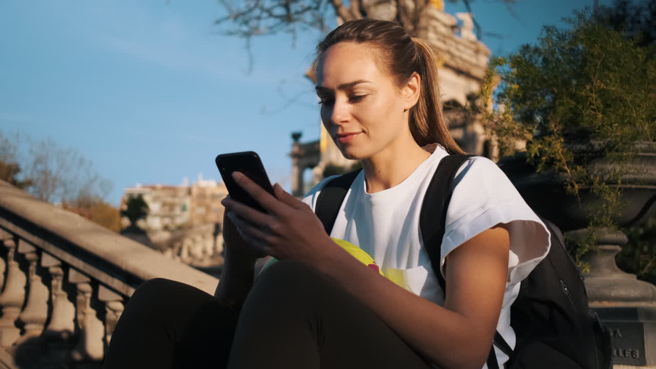 una mujer de fútbol usando un teléfono inteligente, enviando mensajes de texto y esperando a sus amigos.