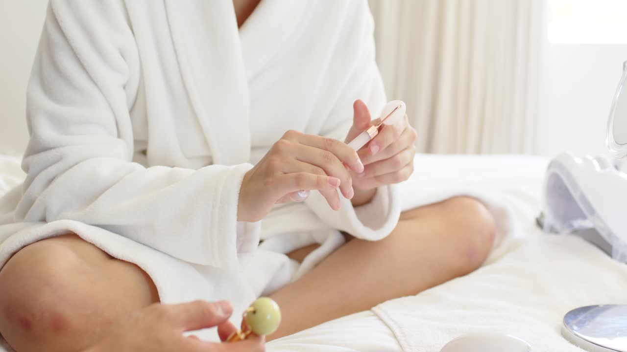 Persona in accappatoio che ispeziona, ruota e prepara un dispositivo rosa sul letto dopo che è apparsa un'altra mano.