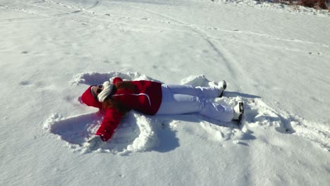 a slow motion side view of a girl making a snow angel in the snow during a bright and sunny winter afternoon outdoors