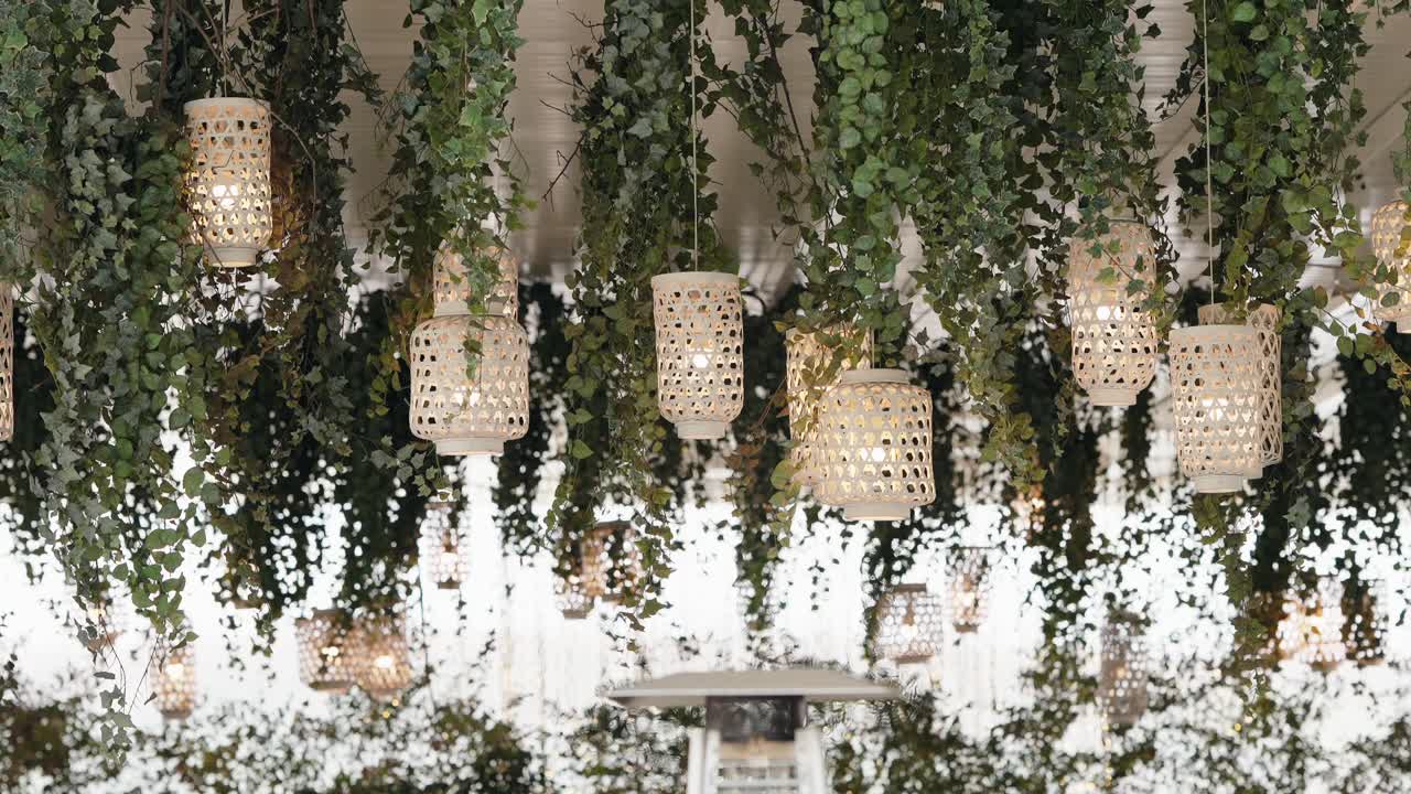 Wicker lanterns and greenery hang from wedding ceiling with soft light