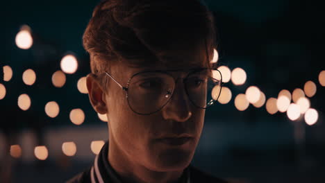 portrait-young-redhead-man-wearing-glasses-on-rooftop-at-night-looking-serious-expression-with-beautiful-party-lights-in-background-urban-youth-concept