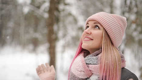 woman in a jacket and hat in slow motion looks at the snow and catches snowflakes smiling