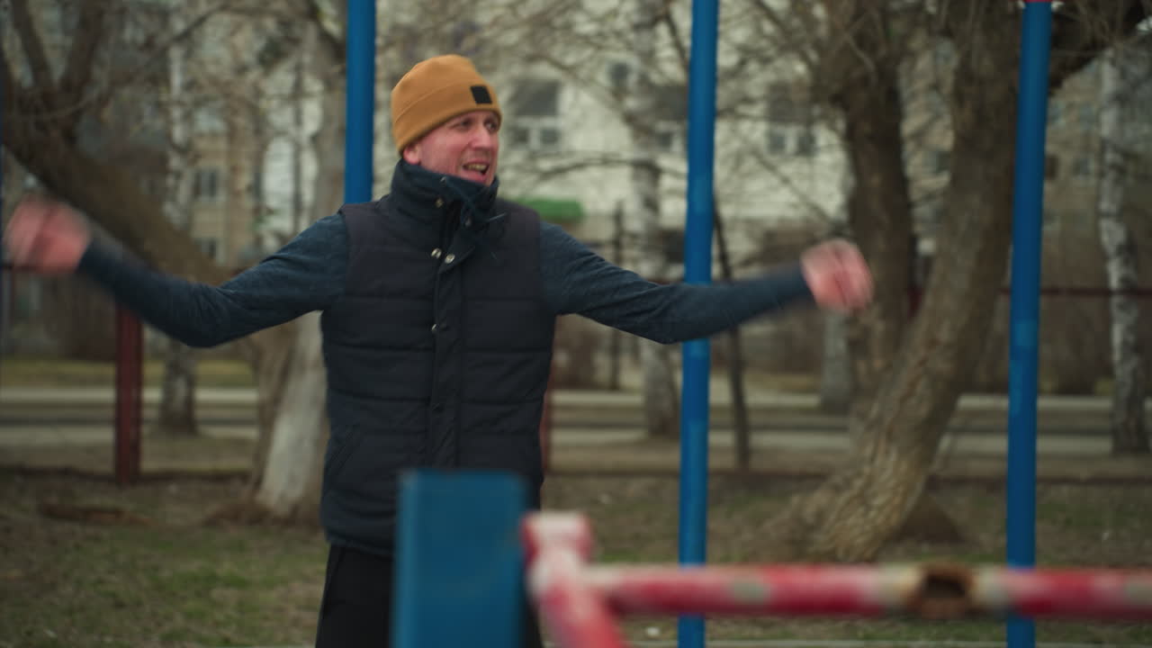 운동을 수행하는 코치의 클로즈업, 아래로 구부러지고 위로, 배경에 재색 자동차가 빠르게 지나가고, 배경에는 건물과 황량한 나무가 있습니다.