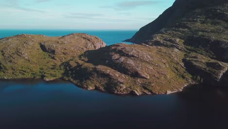 Tilt-up-reveal-drone-shot-of-a-rocky-hill-over-a-lake-in-south-Lofoten