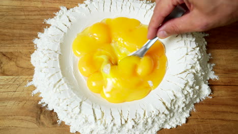 top view of pasta making: perfect egg yolks are beaten inside a well of flour