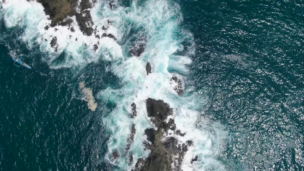 Piccola Barca da Pesca Vicino alla Costa Rocciosa con Forti Onde Oceaniche che la Colpiscono, Ripresa Aerea dall'Alto
