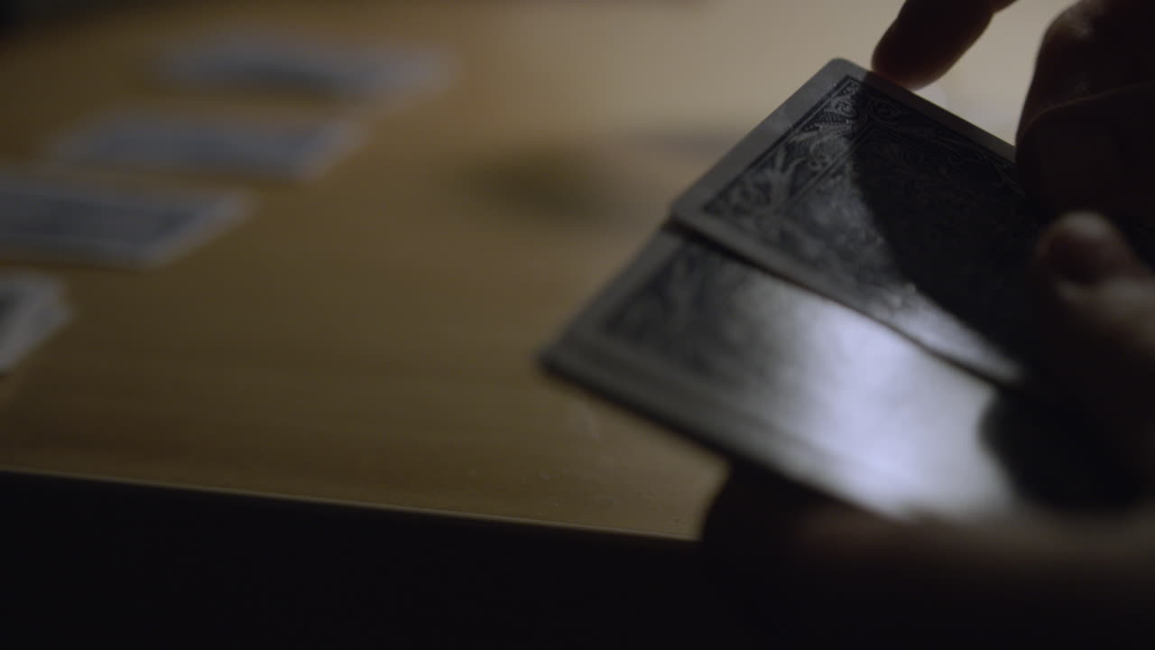 Man deals out playing cards on a table in dim, moody lighting