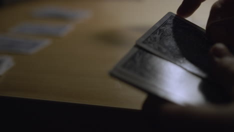 man deals out playing cards on a table in dim, moody lighting