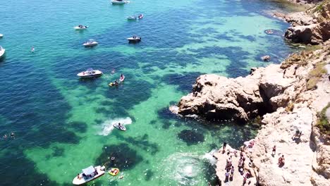 aerial shot of people at the beach jumping of the rocks into the ocean