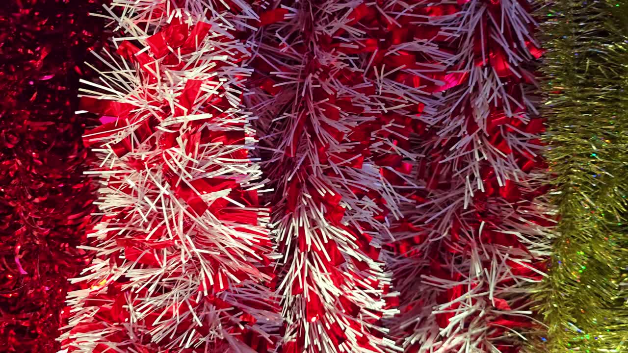 Slow panning shot from left to right showing shiny red, white, and gold Christmas tinsel decorations hanging in a festive display