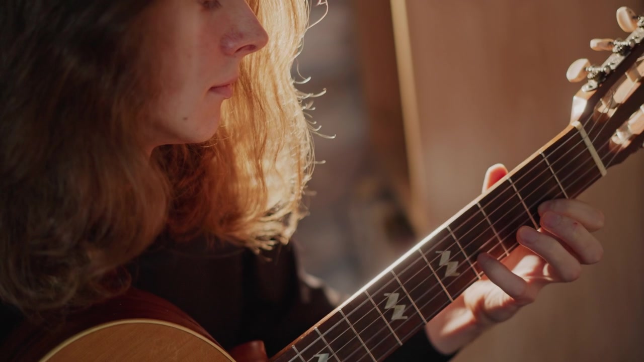 Varmt baggrundsbelyst musiker med blidt guitarspil. Eftertænksom guitarist komponerer i et beroligende musikalsk miljø. Rolig musiker fordybet i at komponere melodier i hyggelige rammer på en musikskole