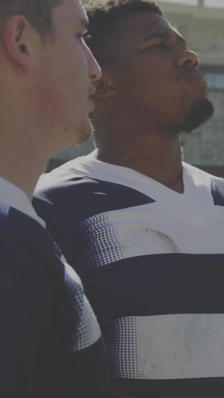 Vertical video: Camera panning rugby duo raising chins sideline, teal hex shifting, prepping play