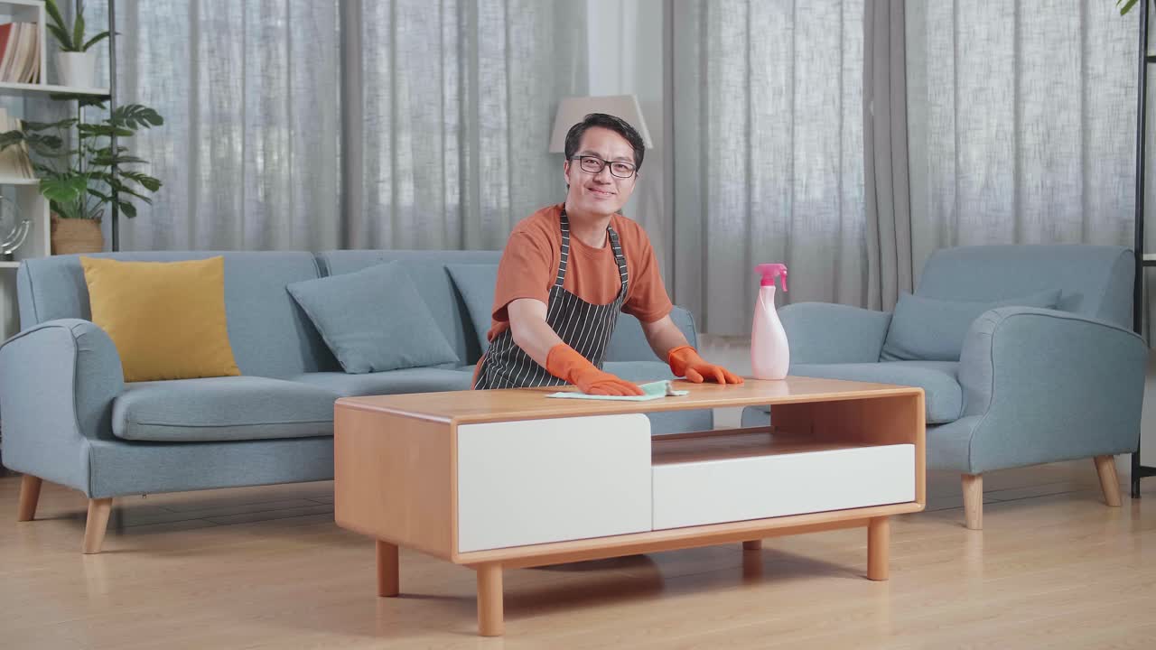 집에서 스프레이로 테이블을 청소하는 동안 미소 짓고 엄지손가락을 보여주는 아시아 남성 집주인