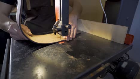 anonymous luthier cutting guitar body on bandsaw in workroom