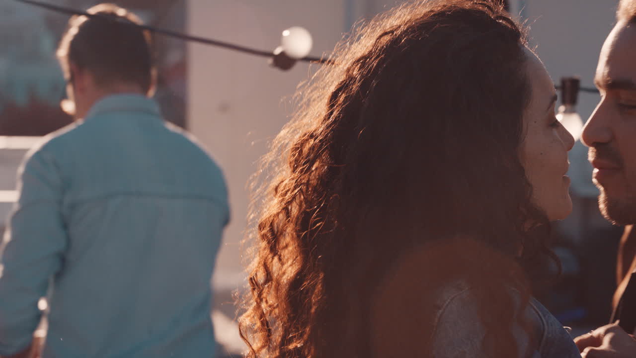 pareja feliz besándose disfrutando de una fiesta en la azotea bailando a música animada compartiendo una relación romántica en una reunión social diversa al atardecer