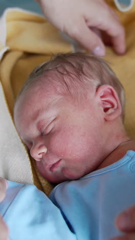 cute tiny baby boy few hours old sleeping in the crib. hands of loving parents caressing the child and he's smiling. vertical video