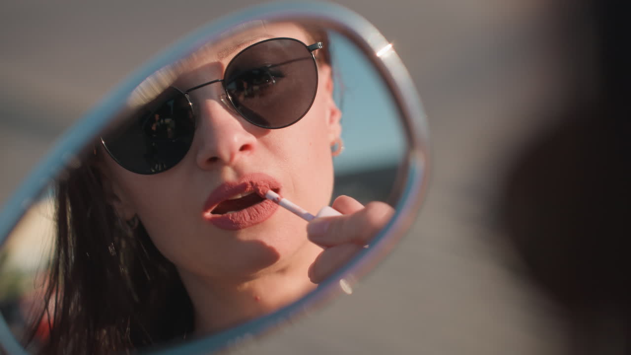 Close up reflection of woman in sunglasses applying lipstick using motorcycle side mirror outdoors with blurred background, capturing elegance, beauty, and confident lifestyle