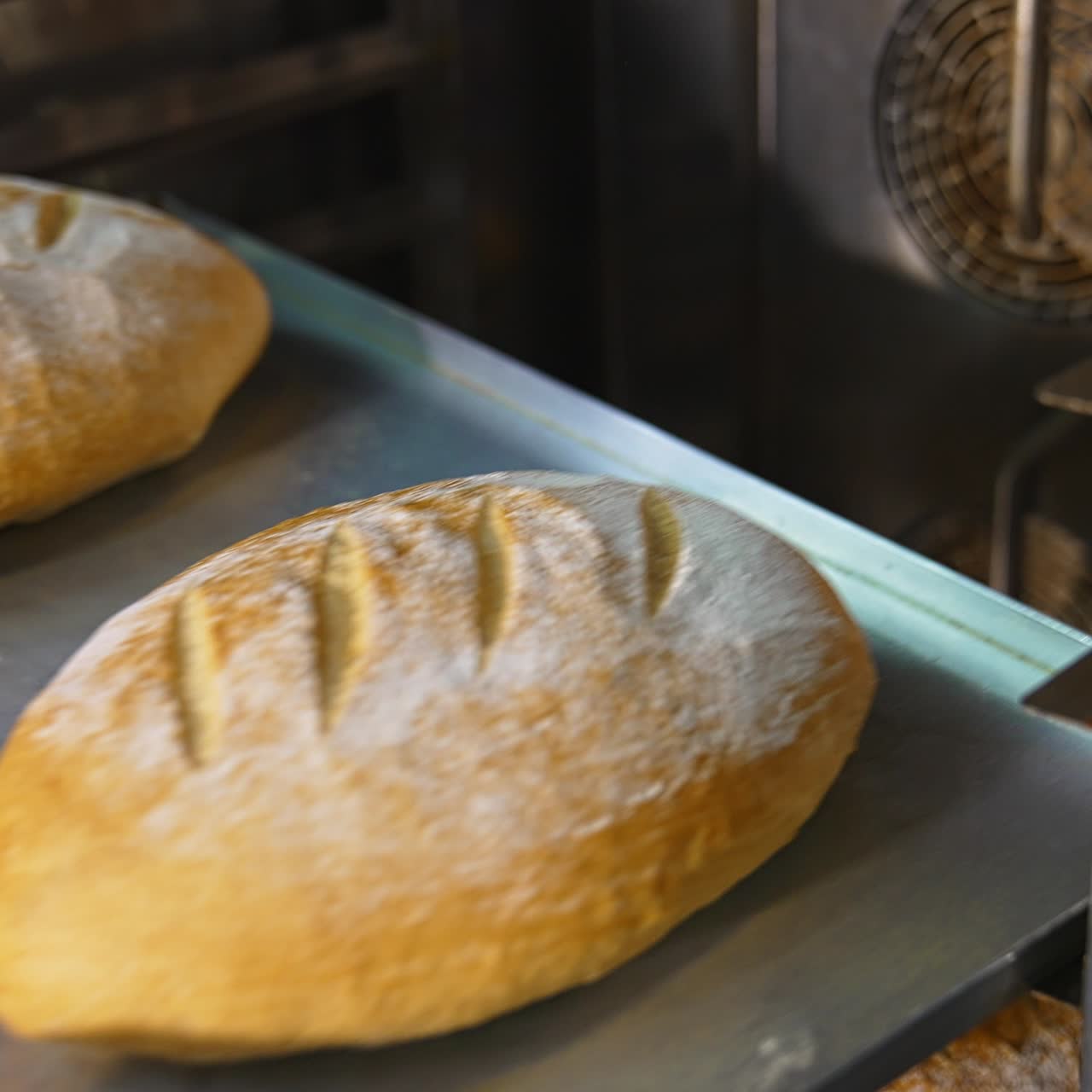 Baker's hands pull freshly-baked loaves from the oven. Making tasty brown bread at bakery. Close up