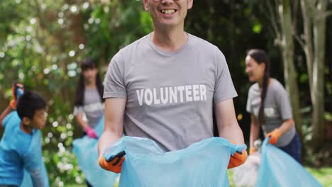 smiling asian man wearing volunteer t shirt holding refuse sack for collecting plastic waste